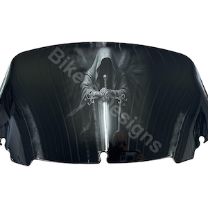 May include: A black motorcycle windshield with a graphic of a hooded figure holding a sword. The figure has wings and is set against a dark background. The text "Bike Designs" is visible.