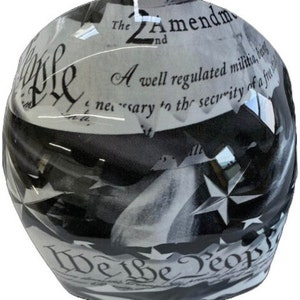 May include: A glossy motorcycle helmet featuring a black and white graphic design. The surface displays text from the 2nd Amendment and the phrase We the People in a decorative script font, interspersed with star shapes across the rounded shell.