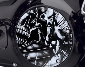 May include: A circular black and white motorcycle derby cover featuring a detailed graphic of a skull and skeletal hand. The design includes the text Ghost Rider printed in white script. The cover is secured with five silver-toned bolts.