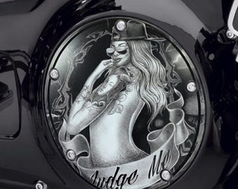 May include: A circular black motorcycle derby cover featuring a monochrome illustration of a person wearing a baseball cap and sunglasses, with a tattoo on their arm. A banner at the bottom displays the text Judge Me in script font.