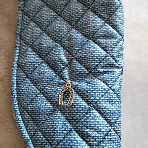 May include: A blue quilted fabric with a silver horseshoe charm attached. The fabric has a denim pattern.