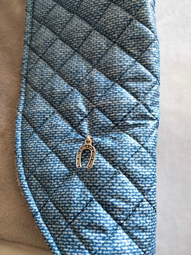 May include: A blue quilted fabric with a silver horseshoe charm attached. The fabric has a denim pattern.