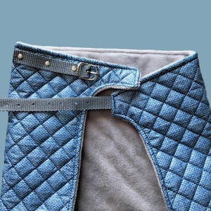 May include: A blue quilted dog harness with a gray adjustable strap and a silver buckle.