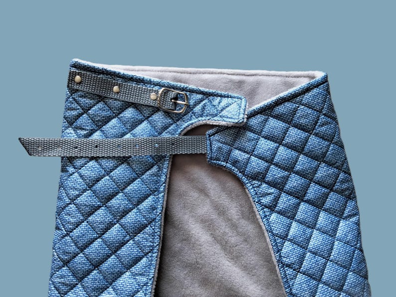May include: A blue quilted dog harness with a gray adjustable strap and a silver buckle.