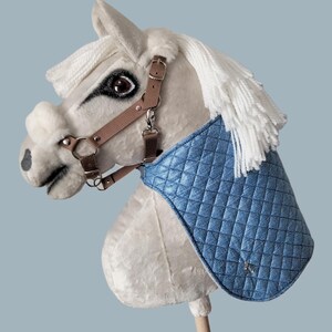 May include: A white plush rocking horse with a brown leather bridle and a blue quilted saddle blanket.