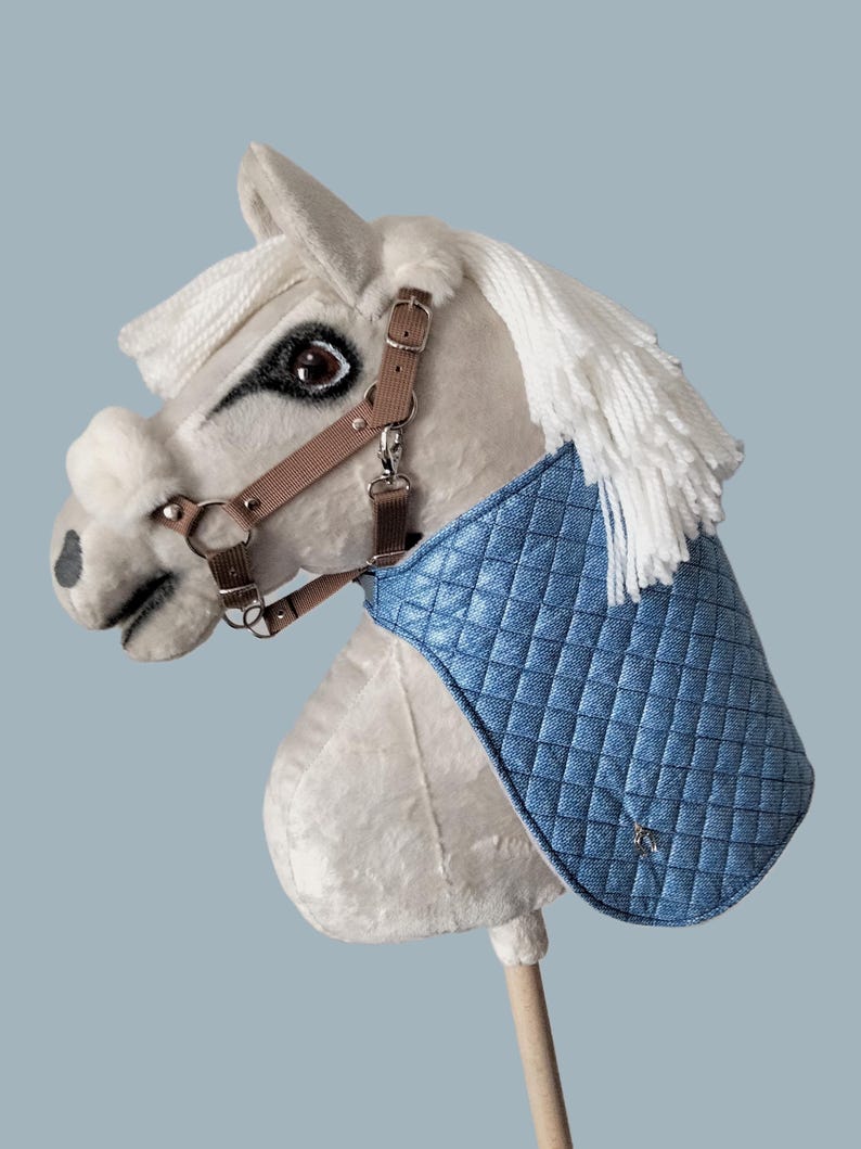 May include: A white plush rocking horse with a brown leather bridle and a blue quilted saddle blanket.