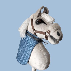 May include: A white plush rocking horse with a blue quilted saddle and brown leather bridle. The horse has a white mane and tail.