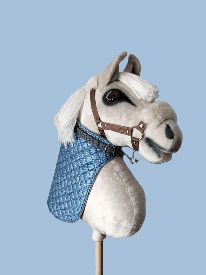 May include: A white plush rocking horse with a blue quilted saddle and brown leather bridle. The horse has a white mane and tail.