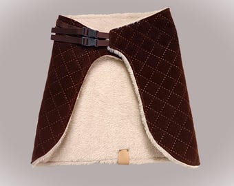 May include: A brown pet bed with a quilted pattern on the exterior and a soft, cream-colored interior. The bed has a buckle closure and a small leather tag. The design is intended to provide comfort and security for pets.