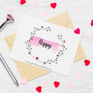 May include: A white card with a pink watercolor background and a black floral wreath with the word "Happy" in the center. The card is surrounded by pink and red hearts on a white wooden surface. The text at the bottom of the card reads "Copyright@PowerDigitalDesign".