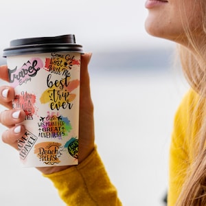 May include: A white paper cup with a black lid and colorful stickers with travel-themed text. The text on the stickers includes "Come Get Lost With Me", "Best Trip Ever", "Life Was Meant For Great Adventures", "Beach Please", and "Love Travel".