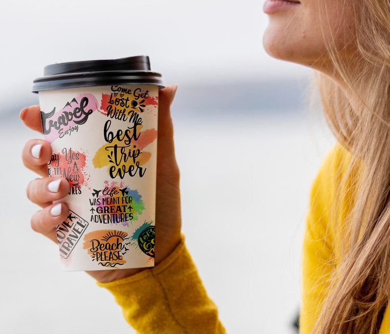 May include: A white paper cup with a black lid and colorful stickers with travel-themed text. The text on the stickers includes "Come Get Lost With Me", "Best Trip Ever", "Life Was Meant For Great Adventures", "Beach Please", and "Love Travel".