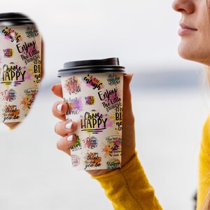 May include: Two white to-go coffee cups with black lids and colorful watercolor-style designs. The cups feature inspirational text, including "Choose Happy", "Enjoy the Little Things", and "As you think, so shall you be".