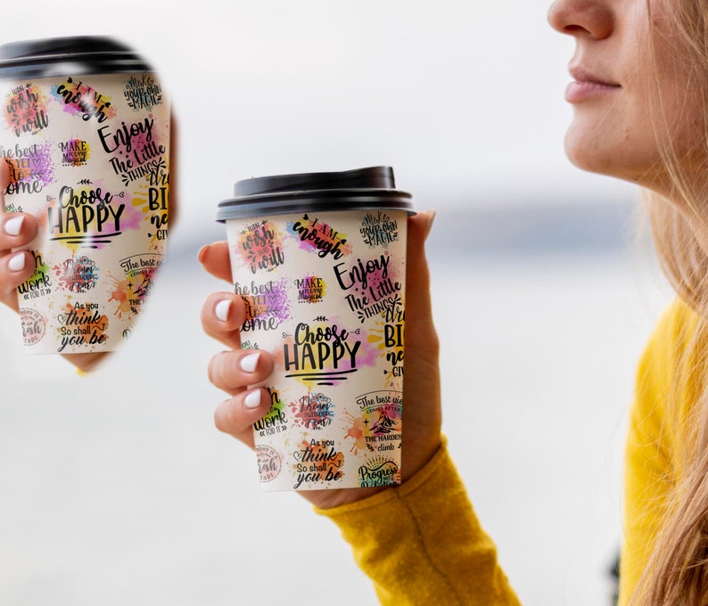 May include: Two white to-go coffee cups with black lids and colorful watercolor-style designs. The cups feature inspirational text, including "Choose Happy", "Enjoy the Little Things", and "As you think, so shall you be".