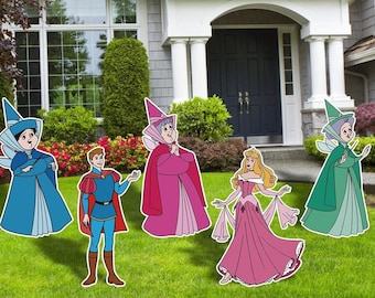 Könnte beinhalten: Fünf Pappfiguren von Charakteren aus dem Disney-Film Dornröschen. Die Figuren sind Aurora, Prinz Philipp, Flora, Fauna und Merryweather. Die Figuren stehen auf einem grünen Rasen vor einem Haus.