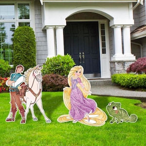 May include: Cardboard cutouts of characters from the animated movie Tangled, including Rapunzel in a purple dress, a horse, a man, and a chameleon. The cutouts are placed on a green lawn in front of a house.