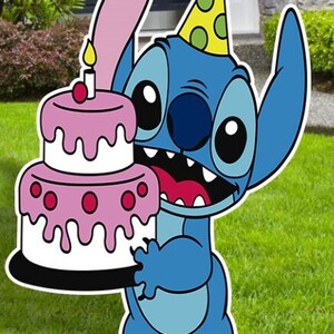 Op de afbeelding: Een blauw cartoonfiguur met een roze oor en een groen-gele feestmuts houdt een roze en witte gelaagde taart vast met een brandende kaars erop.