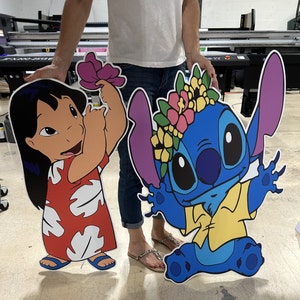 May include: Two large cardboard cutouts of cartoon characters. The character on the left is a girl with long black hair, wearing a red and white dress. The character on the right is a blue alien with large ears, wearing a yellow shirt and a flower crown.