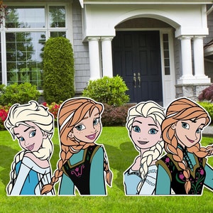 Puede incluir: Cuatro recortes de cart&oacute;n de los personajes de la pel&iacute;cula Frozen. Los recortes son de Elsa y Anna. Elsa lleva un vestido azul y tiene el pelo largo y rubio. Anna lleva un vestido verde y tiene el pelo largo y rojo. Los recortes est&aacute;n de pie en un jard&iacute;n de c&eacute;sped frente a una casa.