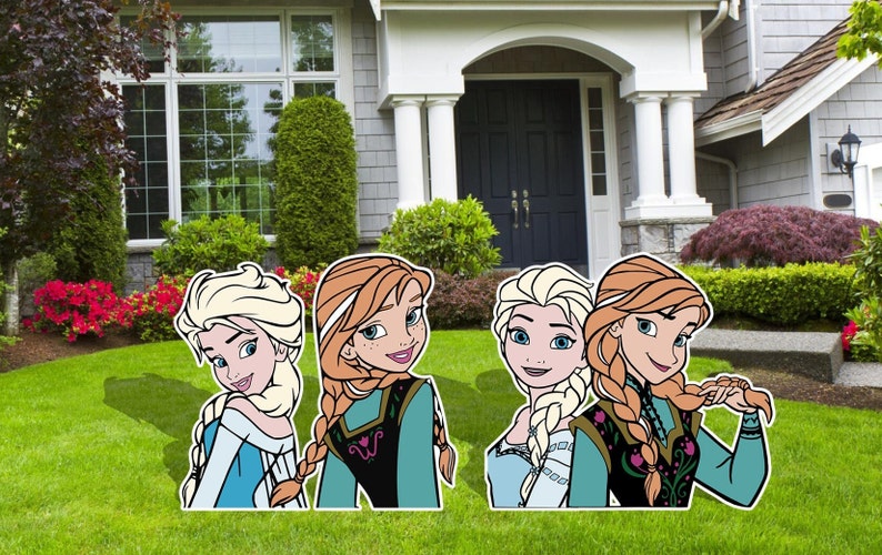 Puede incluir: Cuatro recortes de cart&oacute;n de los personajes de la pel&iacute;cula Frozen. Los recortes son de Elsa y Anna. Elsa lleva un vestido azul y tiene el pelo largo y rubio. Anna lleva un vestido verde y tiene el pelo largo y rojo. Los recortes est&aacute;n de pie en un jard&iacute;n de c&eacute;sped frente a una casa.