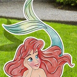 Puede incluir: Una ilustraci&oacute;n de dibujos animados de Ariel, la Sirenita, con el pelo largo y rojo y una cola verde. Lleva un sujetador de concha p&uacute;rpura y mira hacia arriba con una expresi&oacute;n so&ntilde;adora.