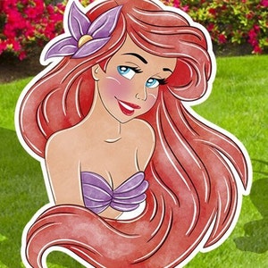 Puede incluir: Una ilustraci&oacute;n de dibujos animados de Ariel, la Sirenita, con el pelo largo y rojo, un sujetador de concha de mar morado y una flor morada en el pelo.