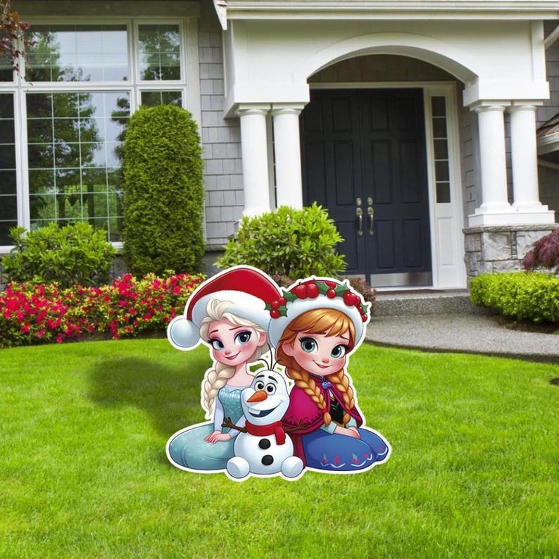 Puede incluir: Decoraci&oacute;n exterior colorida con los personajes de dibujos animados Elsa, Anna y Olaf de la pel&iacute;cula Frozen. Elsa lleva un gorro de Pap&aacute; Noel, Anna una corona de bayas y Olaf una bufanda roja. Los personajes est&aacute;n sobre c&eacute;sped verde.