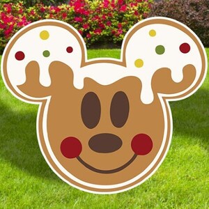 Puede incluir: Un recorte de cabeza de Mickey Mouse de jengibre con glaseado blanco y chispas rojas y verdes. El recorte es marr&oacute;n y tiene una cara sonriente con ojos negros y una nariz marr&oacute;n.
