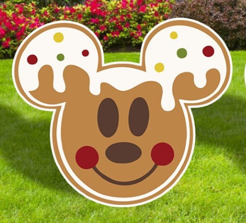 Puede incluir: Un recorte de cabeza de Mickey Mouse de jengibre con glaseado blanco y chispas rojas y verdes. El recorte es marr&oacute;n y tiene una cara sonriente con ojos negros y una nariz marr&oacute;n.