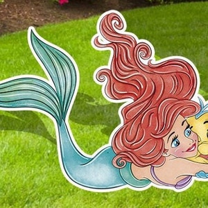 Puede incluir: Un recorte de Ariel, la Sirenita, con cabello rojo y cola azul, abrazando a un Flounder amarillo. El recorte est&aacute; sobre un fondo de hierba verde.