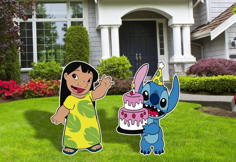 Op de afbeelding: Lilo en Stitch verjaardagsparty decoraties. Lilo draagt een gele jurk met groene bladeren en zwaait. Stitch houdt een roze en witte taart vast met een enkele kaars en draagt een groen-gele feestmuts.