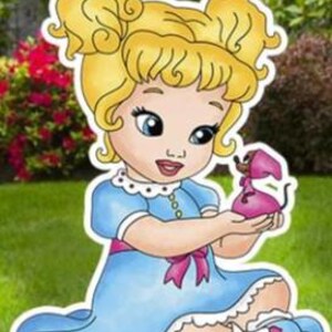 May include: A cartoon-style cutout of a young child with blonde hair in two buns, wearing a light blue dress with a pink sash and white trim. The child is holding a small pink mouse figure in their hands. The illustration features bold outlines.