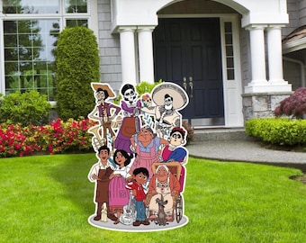 May include: A colorful cardboard cutout of the characters from the animated movie Coco. The characters are standing in front of a house with a green lawn. The characters include Miguel, Hector, Mama Imelda, Dante, and others.