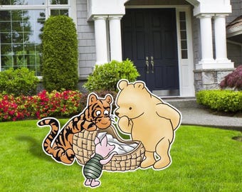 May include: A yard decoration featuring Winnie the Pooh, Tigger, and Piglet gathered around a basket. The characters are in a grassy yard in front of a house with a dark blue door and white columns. The characters are in a cartoon style.