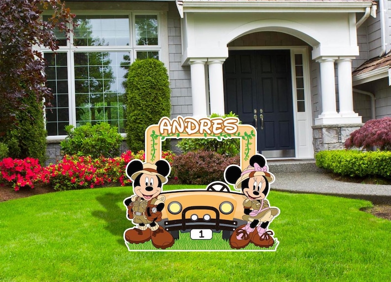 May include: A photo booth cutout featuring Mickey and Minnie Mouse dressed in safari outfits. The cutout is decorated with green vines and the name "ANDRES" is written at the top. A yellow jeep is in the middle of the cutout.
