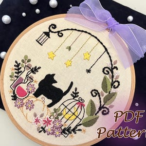 May include: Embroidered hoop art featuring a black cat, a birdcage, and floral designs. The hoop is decorated with a purple ribbon. The text "PDF Pattern" is visible in the bottom right corner.