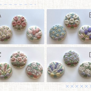 Puede incluir: Cuatro ramos de flores bordados en botones redondos de tela blanca. Los ramos son en tonos de rosa, blanco, azul y morado. Los botones est&aacute;n dispuestos en una cuadr&iacute;cula con las letras A, B, C y D etiquetando cada fila.
