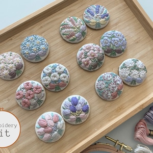 Puede incluir: Un conjunto de 10 kits de bordado con diferentes dise&ntilde;os florales. Cada kit incluye una pieza de tela precortada con un dise&ntilde;o floral, hilo de bordar y una aguja. Los kits est&aacute;n dispuestos en una bandeja de madera.