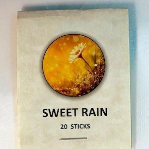 May include: A package of brown incense sticks with a label that says "Sweet Rain" and "20 Sticks". The label also features a yellow and white flower with a yellow background.