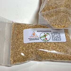 Puede incluir: Una bolsa de pl&aacute;stico transparente llena de hierba de Ashwagandha seca de color marr&oacute;n claro. La bolsa tiene una etiqueta con el texto "Ashwagandha" y "AlchemyFlame" con una peque&ntilde;a imagen de una planta de bayas rojas.