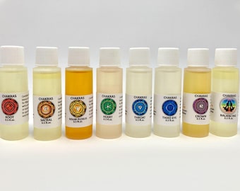 May include: A collection of eight small bottles, each labeled with a chakra name and symbol. The bottles contain various colored liquids, ranging from clear to yellow and orange. The labels include the words "Root," "Sacral," "Solar Plexus," "Heart," "Throat," "Third Eye," "Crown," and "Balancing."