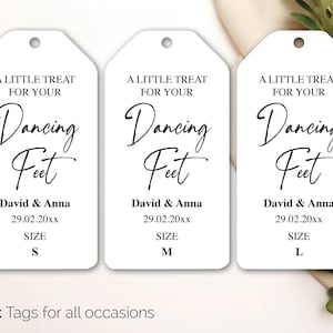 May include: Three white gift tags with rounded tops. Each tag has the text "A LITTLE TREAT FOR YOUR Dancing Feet" in black script. Below is "David & Anna 29.02.20xx" and size options S, M, and L.