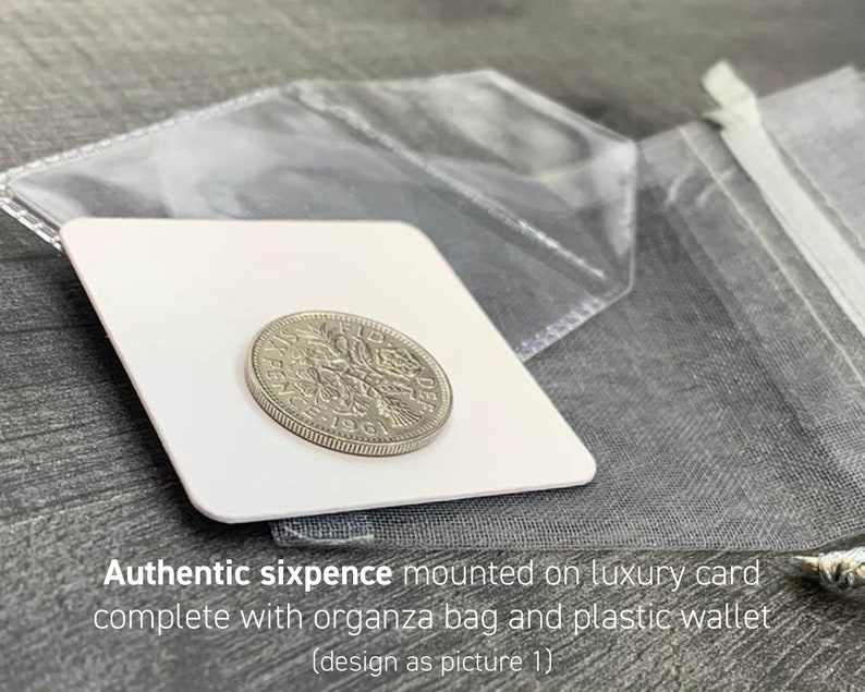 May include: A silver sixpence coin from 1961 is displayed on a white card, accompanied by a clear plastic wallet and a gray organza bag. The text "Authentic sixpence mounted on luxury card complete with organza bag and plastic wallet" is visible.