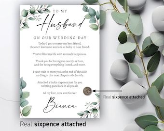 May include: A wedding card with the text "To My Husband" and a personal message. The card is decorated with green eucalyptus leaves and includes a real sixpence coin. The card is white with black script.