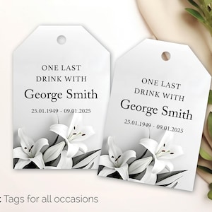 May include: Two white gift tags with the text "ONE LAST DRINK WITH George Smith" and dates. Each tag features white lily flowers at the bottom. The phrase "Gift Tags for all occasions" is at the bottom.