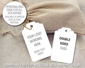 May include: White personalized tags with scalloped edges, featuring text like "YOUR LOGO WORDING HERE" and "DOUBLE SIDED TAGS." A beige drawstring bag is in the background. The tags are available in various sizes and card materials.