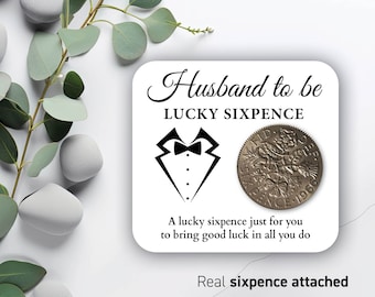 May include: A white card with black text that reads "Husband to be Lucky Sixpence". A black and white illustration of a tuxedo is on the card. A silver sixpence coin is attached to the card. The text at the bottom of the card reads "A lucky sixpence just for you to bring good luck in all you do. Real sixpence attached."