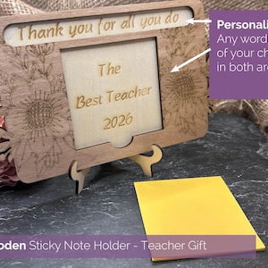 Peut inclure: Un porte-notes adhésives rectangulaire en bois avec des motifs floraux gravés au laser sur les côtés. Le panneau central affiche le texte Thank you for all you do, The Best Teacher, et 2026. Le support repose sur un petit socle en bois.