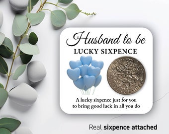 May include: A white card with the text "Husband to be Lucky Sixpence" and a blue heart balloon illustration. A silver sixpence coin is attached to the card with the text "A lucky sixpence just for you to bring good luck in all you do. Real sixpence attached."