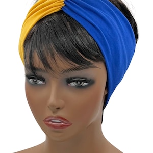 May include: A two-tone headband in yellow and blue. The headband is made of a soft, stretchy fabric and is designed to be worn around the head. The yellow section is on the left side, and the blue section is on the right.
